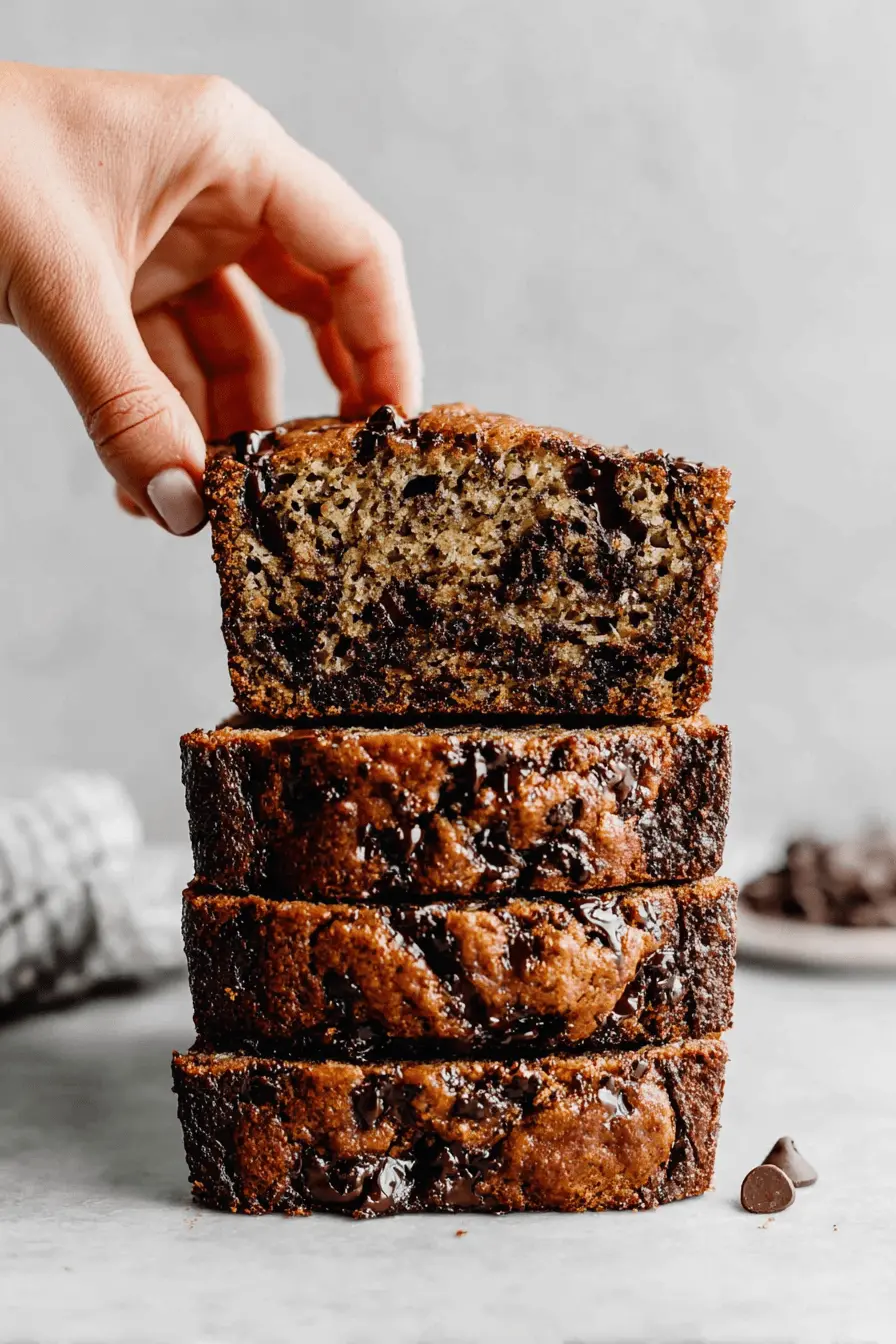 Unbelievably Moist Chocolat Banana Bread 2 Hand reaching for a slice of moist, stacked chocolat banana bread with dark chocolate chips.