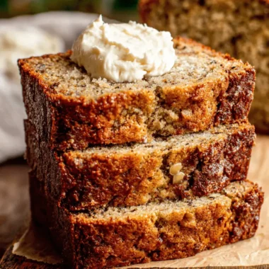 Amazing Sour Cream Banana Bread: So Moist! 4 Stacked slices of moist, frosted sour cream banana bread on a rustic wooden cutting board.