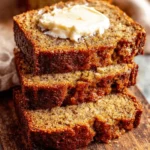 Amazing Sour Cream Banana Bread Recipe 6 Three stacked slices of rich, moist sour cream banana bread topped with melting butter on a rustic wooden cutting board.