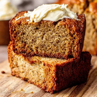 Foolproof Sour Cream Banana Bread Recipe 4 Close-up of two moist slices of sour cream banana bread, stacked on a wooden board with a creamy topping.