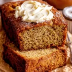 Magic Sour Cream Banana Bread Recipe 5 Close-up of moist, golden-brown sour cream banana bread slices with creamy frosting and coarse sugar on crinkled brown paper.