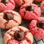 Amazing Strawberry Kiss Cookies Recipe 9 Overhead close-up of sparkling pink **strawberry kiss cookies** topped with rich chocolate centers on a black cooling rack.
