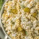 The Ultimate Dill Pickle Pasta Salad 9 Top-down view of a creamy dill pickle pasta salad with fusilli, carrots, and fresh dill in a light blue bowl on a rustic wooden table, ready to be served.