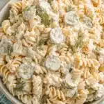 Wonderful Dill Pickle Pasta Salad: Creamy & Tangy 8 A close-up, top-down view of a creamy dill pickle pasta salad with fusilli pasta, pickle slices, shredded carrots, and fresh dill garnish in a ceramic bowl.