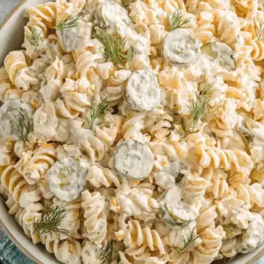 Wonderful Dill Pickle Pasta Salad: Creamy & Tangy 4 A close-up, top-down view of a creamy dill pickle pasta salad with fusilli pasta, pickle slices, shredded carrots, and fresh dill garnish in a ceramic bowl.
