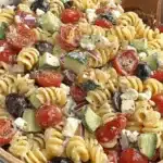 Amazing Pasta Salad with Italian Dressing 9 Overhead view of a vibrant rotini pasta salad with Italian dressing, cherry tomatoes, cucumbers, olives, feta, and red onion in a rustic bowl.