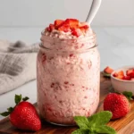 Amazing Strawberry Overnight Oats for Easy Mornings 7 Mason jar filled with creamy strawberry overnight oats, garnished with fresh whole and diced strawberries and a sprig of mint.