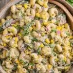 The Ultimate Foolproof Corn Pasta Salad 7 A close-up of a rustic bowl filled with creamy corn pasta salad, featuring elbow macaroni, bright yellow corn kernels, red onion, and fresh green herbs.
