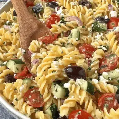Quick & Easy Rotini Pasta Salad Recipe 3 Overhead view of a vibrant Greek rotini pasta salad in a white bowl with a wooden server.