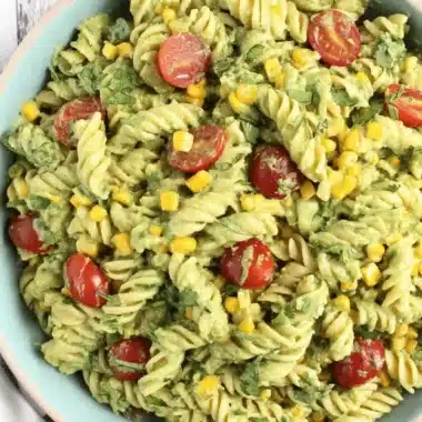 Vibrant Avocado Pasta Salad: Easy & Creamy Recipe 4 Close-up overhead view of a creamy avocado pasta salad with rotini, corn, cherry tomatoes, and cilantro in a light blue bowl on a wooden surface.
