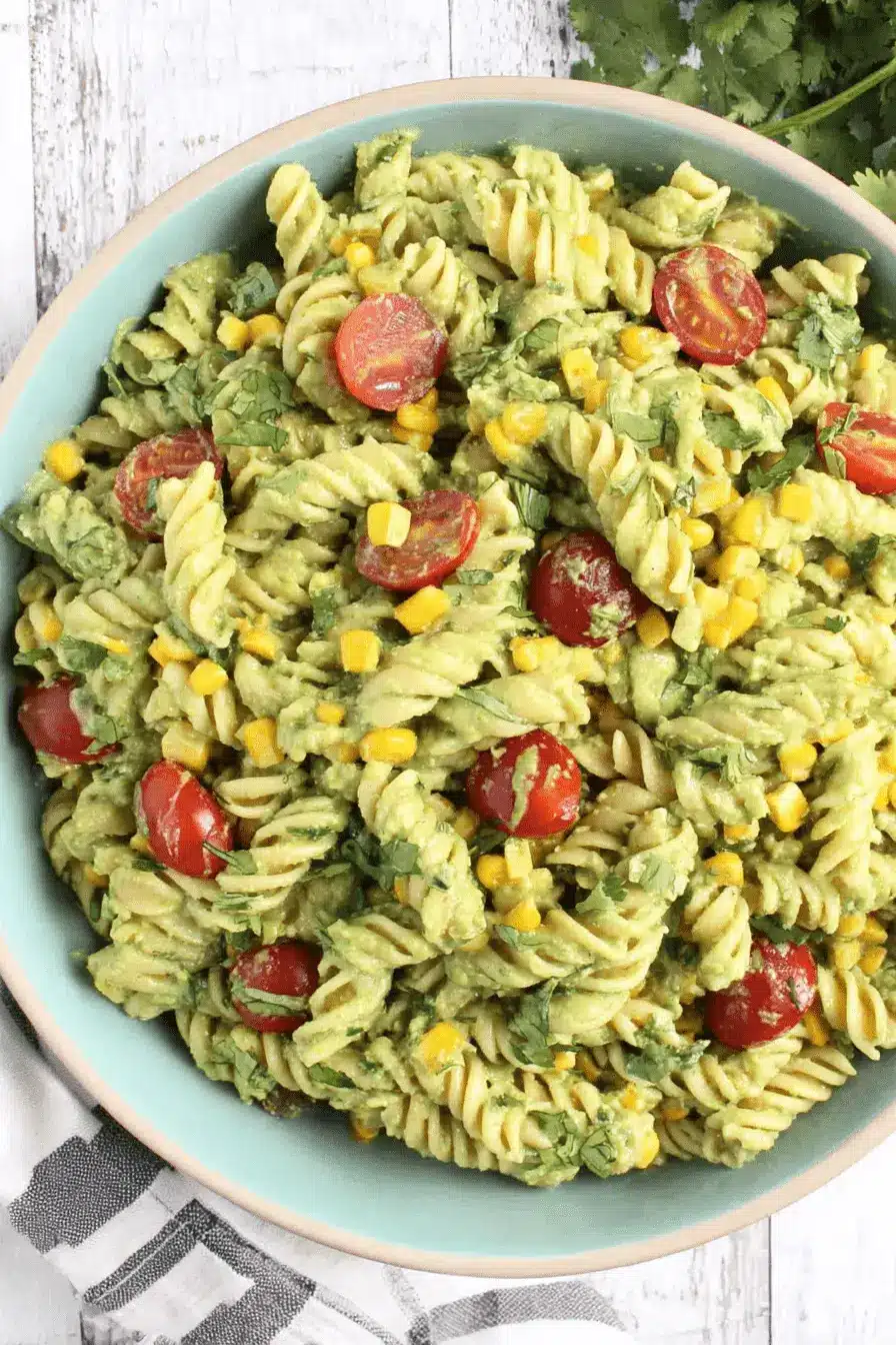 Vibrant Avocado Pasta Salad: Easy & Creamy Recipe 2 Close-up overhead view of a creamy avocado pasta salad with rotini, corn, cherry tomatoes, and cilantro in a light blue bowl on a wooden surface.
