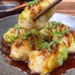 Amazing Homemade Cabbage Dumplings Recipe 7 Close-up of vibrant green cabbage dumplings in a dark ceramic bowl, glistening with savory sauce and topped with green onions, held by chopsticks.