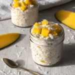 Easy Mango Coconut Overnight Oats for Quick Mornings 5 Two servings of creamy mango coconut overnight oats in clear glass jars, topped with fresh diced mango and shredded coconut flakes.