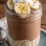 Amazing Mocha Overnight Oats Recipe 5 Close-up of layered mocha overnight oats topped with fresh banana, cream, and seeds in a clear glass jar.