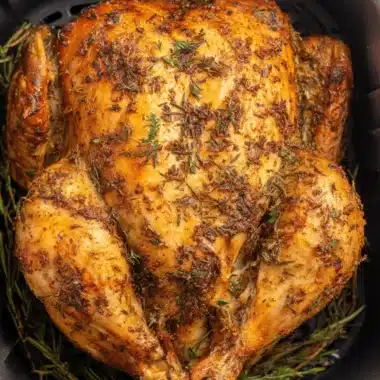 Perfect Air Fryer Whole Chicken Recipe 3 Close-up of a golden brown, herb-seasoned air fryer whole chicken inside the black air fryer basket.