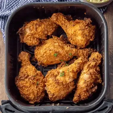 Amazing Air Fryer Fried Chicken Recipe 3 Golden-brown, crispy air fryer fried chicken drumsticks served in a black basket with a side of creamy coleslaw on a wooden table.