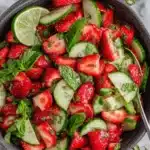 Ultimate Refreshing Cucumber Strawberry Salad 9 Top-down view of a fresh Cucumber Strawberry Salad with mint and lime slices in a dark gray bowl, ready to be served.