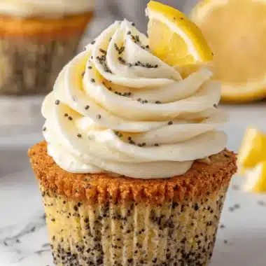 Amazing Lemon Poppy Seed Cupcakes Recipe 4 Close-up of a single, perfectly frosted lemon poppy seed cupcake garnished with a fresh lemon slice on a marble surface.