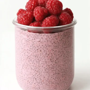 The Ultimate Vegan Raspberry Chia Pudding for Easy Mornings 3 Clear glass jar filled with pink Vegan Raspberry Chia Pudding and topped with fresh red raspberries.