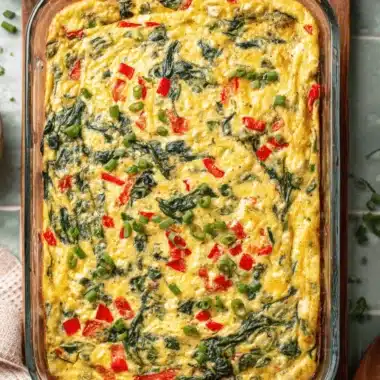The Ultimate Cottage Cheese and Veggie Bake 4 Top-down view of a freshly baked, rectangular Cottage Cheese and Veggie Bake with spinach and red peppers, garnished with green onions in a glass dish.