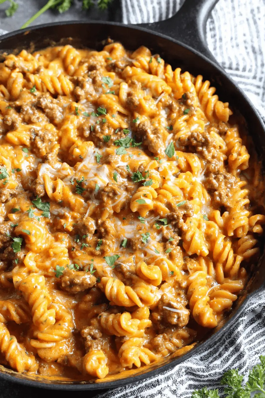 Amazing One-Pot Creamy Beef Pasta Recipe 2 Hearty cast iron skillet filled with garnished rotini Creamy Beef Pasta, viewed from overhead.