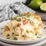 Easy White Queso Chicken Enchiladas Recipe 7 Freshly baked white queso chicken enchiladas serving on a speckled plate, garnished with cilantro and golden melted cheese.