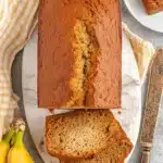 Ultimate One Bowl Banana Bread Recipe 7 Top-down view of a moist, golden-brown loaf of one bowl banana bread on a marble board with two cut slices and ripe bananas.