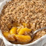 Simple Peach Crisp with Fresh Peaches: Fantastic Flavor 9 A close-up of a golden-brown peach crisp with fresh peaches, served in a white ceramic dish with a spoon.
