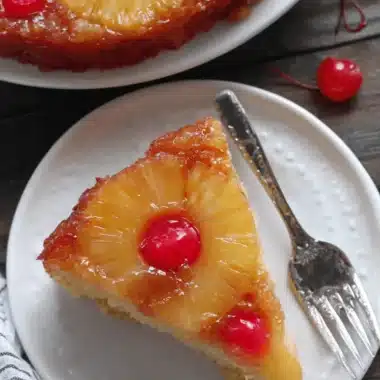 Ultimate Pineapple Upside Down Cake with Box Cake 3 Close-up of a delicious slice of pineapple upside down cake with box cake, featuring caramelized pineapple and maraschino cherries on a white plate with a fork.