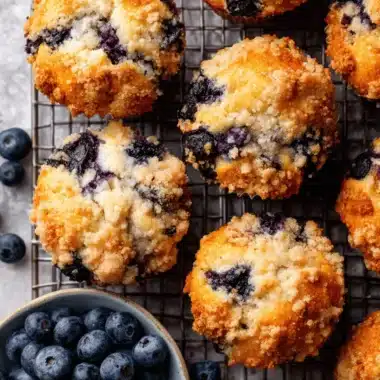 Ultimate Bakery Style Blueberry Muffins 4 Freshly baked bakery style blueberry muffins with a crumbly streusel topping, presented on a cooling rack.