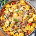 Amazing Garlic Parmesan Steak Tortellini 6 A top-down view of a rustic blue casserole dish overflowing with delicious Garlic Parmesan Steak Tortellini, garnished with fresh basil and grated cheese.