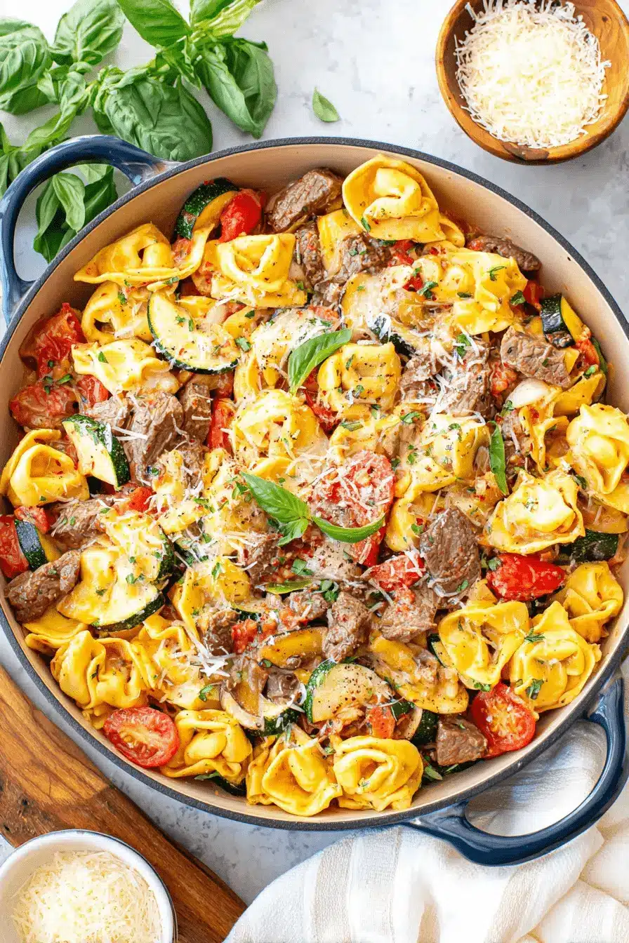 Amazing Garlic Parmesan Steak Tortellini 2 A top-down view of a rustic blue casserole dish overflowing with delicious Garlic Parmesan Steak Tortellini, garnished with fresh basil and grated cheese.