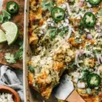 The Ultimate Salsa Verde Chicken Casserole 5 A creamy, cheesy salsa verde chicken casserole, fresh from the oven, garnished with jalapeños, red onion, and cilantro, with a serving being lifted by a spatula.