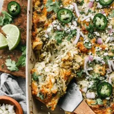 The Ultimate Salsa Verde Chicken Casserole 4 A creamy, cheesy salsa verde chicken casserole, fresh from the oven, garnished with jalapeños, red onion, and cilantro, with a serving being lifted by a spatula.