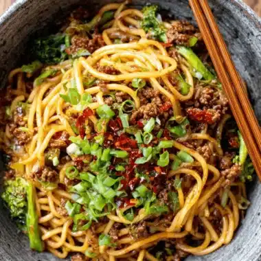 Fantastic Sticky Beef Noodles in Under 30 Minutes 3 Close-up of delicious sticky beef noodles with broccoli and green onions in a rustic bowl.