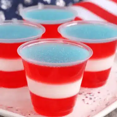 Amazing Foolproof Red White and Blue Jello Shots 4 Four festive red white and blue jello shots layered on a platter with an American flag background.