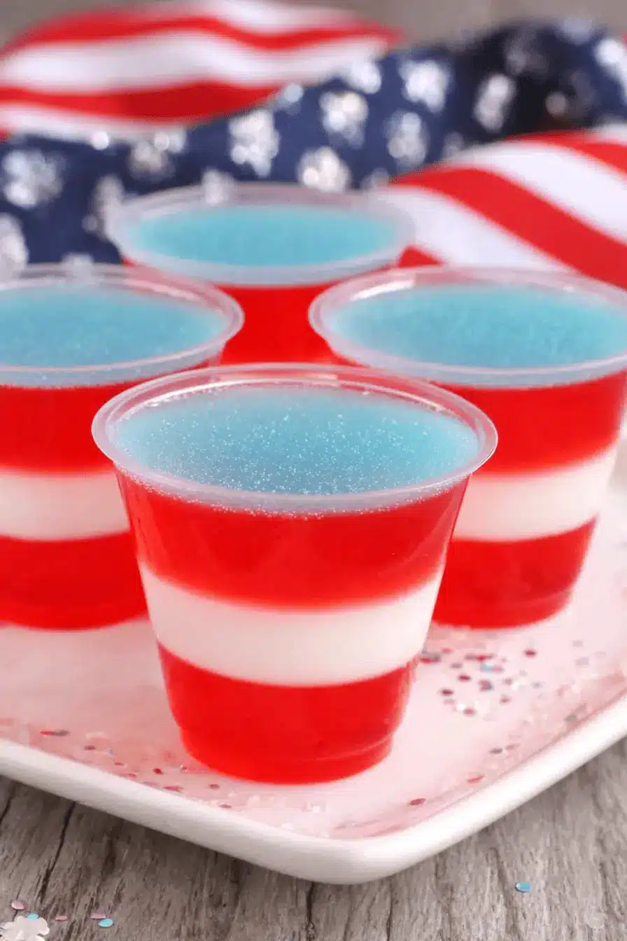 Amazing Foolproof Red White and Blue Jello Shots 2 Four festive red white and blue jello shots layered on a platter with an American flag background.