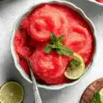 Ultimate Watermelon Sorbet: Easy 5-Minute Treat 8 Vibrant watermelon sorbet in a blue bowl, garnished with fresh mint and lime, with watermelon slices and additional garnishes on a wooden board.