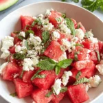 Vibrant Watermelon Feta Mint Salad Recipe 5 A refreshing watermelon feta mint salad in a white bowl, featuring cubed watermelon, crumbled feta, and fresh mint leaves, garnished with black pepper.