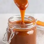 The Ultimate Foolproof Miso Caramel Sauce 5 Close-up of glossy miso caramel sauce dripping from a spoon into a rustic glass jar.