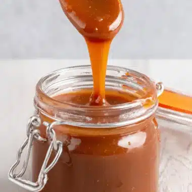 The Ultimate Foolproof Miso Caramel Sauce 4 Close-up of glossy miso caramel sauce dripping from a spoon into a rustic glass jar.