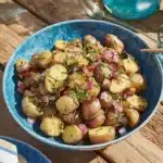 Ultimate Warm German Potato Salad Recipe 9 Close-up of rustic German potato salad with bacon, red onion, and chives in a blue bowl.