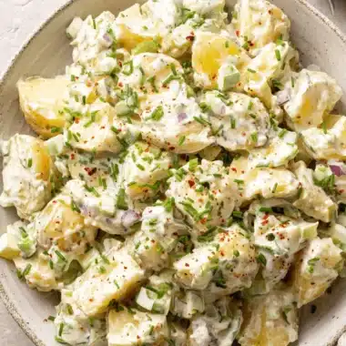 Amazing Potato Salad with Egg Recipe 3 Close-up of a rustic bowl of creamy homemade potato salad with egg, garnished with chives and red pepper flakes.