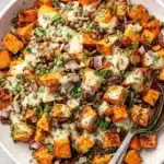 Vibrant Sweet Potato Salad Recipe for Any Meal 7 A vibrant sweet potato salad recipe in a shallow off-white bowl, featuring roasted sweet potatoes, lentils, red onion, dried cranberries, pumpkin seeds, fresh herbs, and a creamy dressing, with silver serving spoons.
