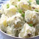 Ultimate Vibrant Greek Potato Salad 6 Close-up of a creamy homemade greek potato salad with green onions and a hint of red onion, served in a bowl on a checkered cloth.