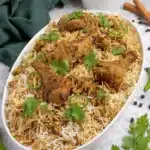 Foolproof Chicken Pulao Recipe for Fluffy Rice 5 Overhead shot of a generously portioned, aromatic chicken pulao recipe on a white platter, garnished with cilantro and green chilies.