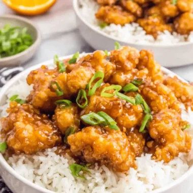 The Ultimate Panda Express Orange Chicken Recipe 4 Two bowls of delicious Panda Express orange chicken served over white rice, garnished with green onions and fresh orange slices.