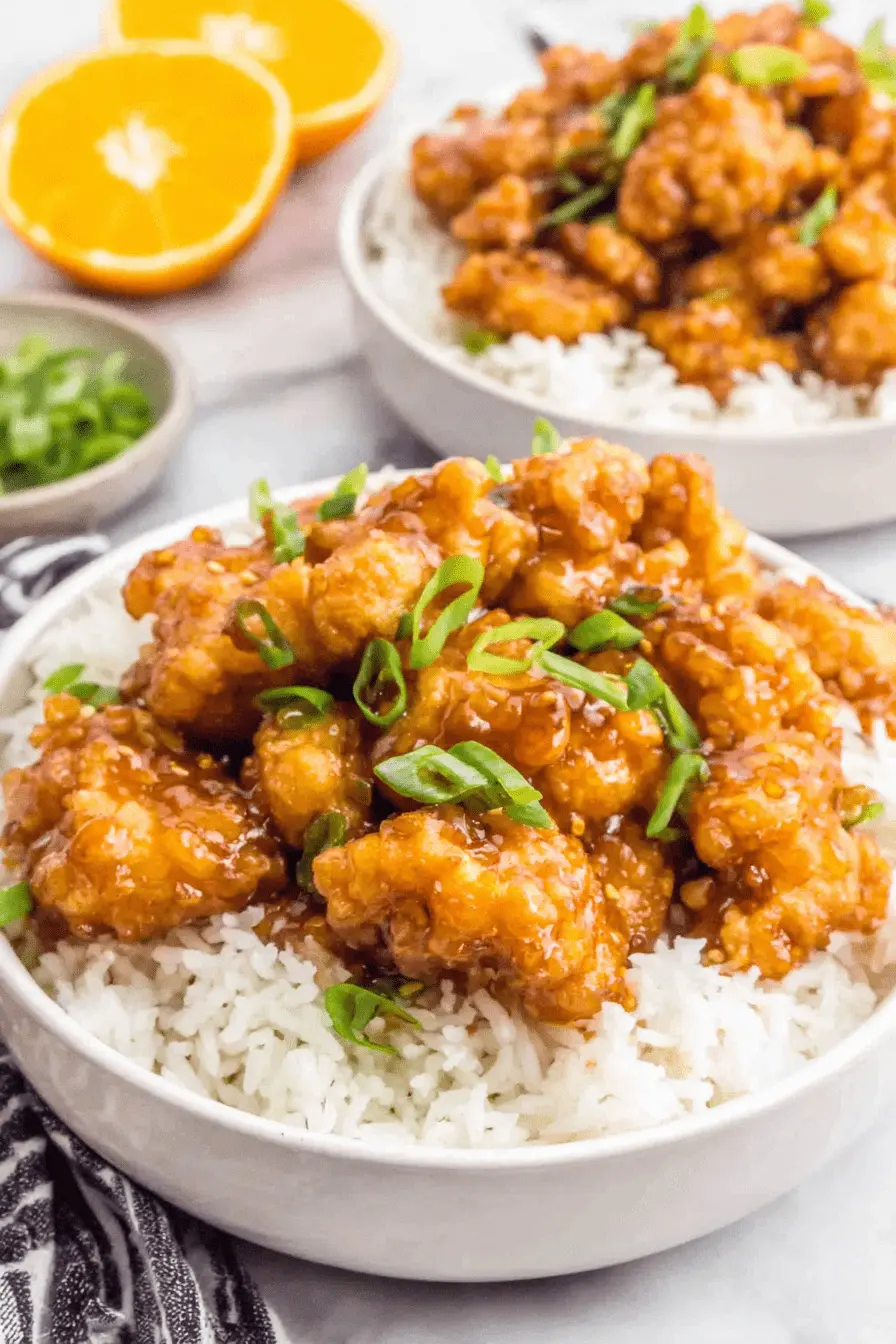 The Ultimate Panda Express Orange Chicken Recipe 2 Two bowls of delicious Panda Express orange chicken served over white rice, garnished with green onions and fresh orange slices.