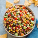 Vibrant & Easy Cowboy Caviar Recipe 7 A vibrant bowl of cowboy caviar recipe, also known as Texas Caviar, with black beans, corn, red peppers, avocado, and cilantro, served with tortilla chips and lime wedges.