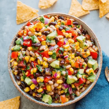 Vibrant & Easy Cowboy Caviar Recipe 3 A vibrant bowl of cowboy caviar recipe, also known as Texas Caviar, with black beans, corn, red peppers, avocado, and cilantro, served with tortilla chips and lime wedges.